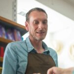 A male store clerk assisting a customer with a payment transaction in a retail shop setting.