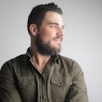 A thoughtful, bearded man in a green shirt looking away against a white studio background.
